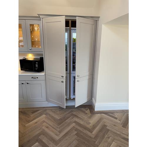 Custom built full height light grey kitchen cabinets with open doors showing built in fridge freezer 500x500