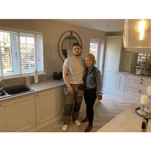 Two happy people standing in fitted kitchen with cream cabinets and grey worktops 500x500